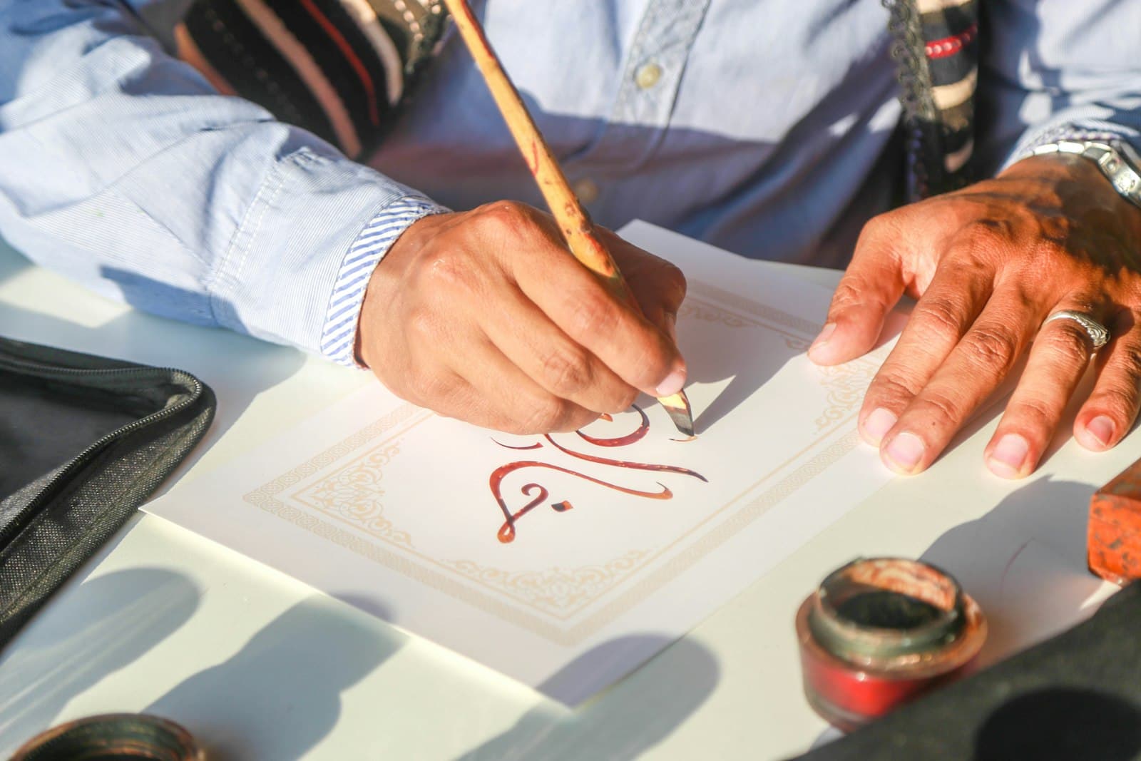 A calligrapher writing Arabic script in red ink with a reed pen