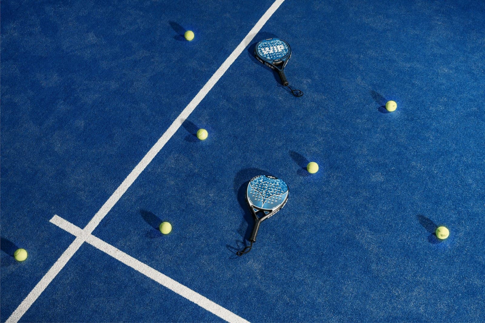 Two padel bats and scattered balls on a blue court, seen from above