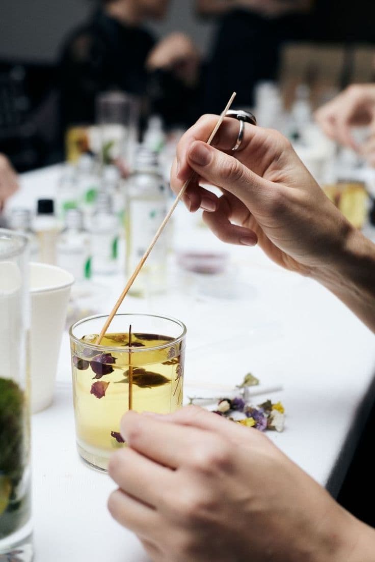 Hands stirring a candle wick into a glass vessel at a workshop table