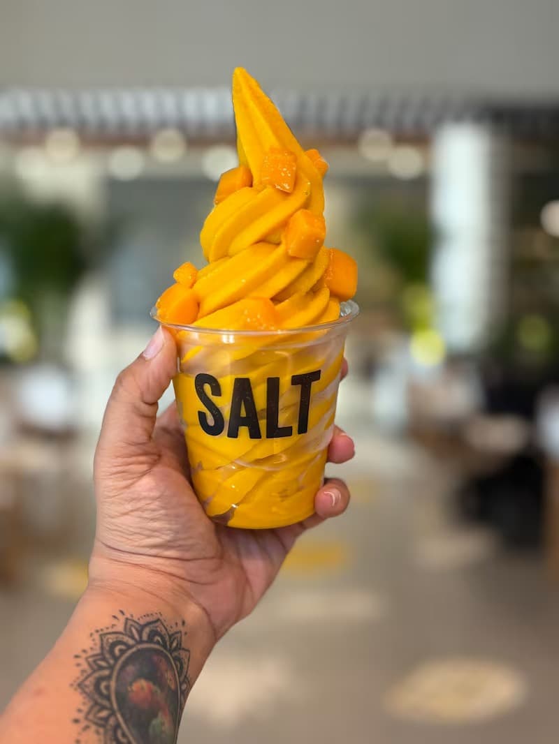 A hand holding SALT’s signature mango softie in a branded cup