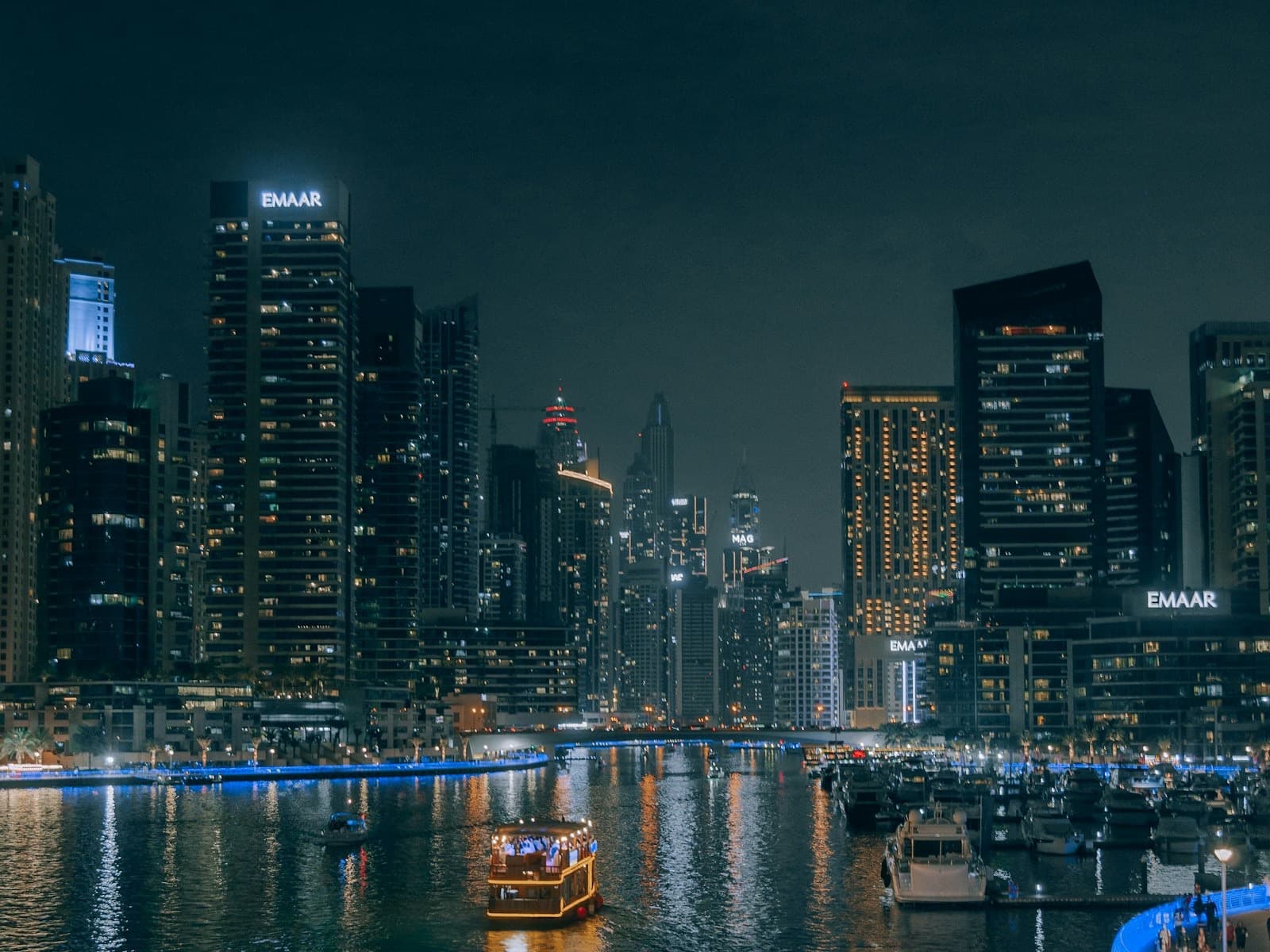 A lantern-lit wooden dhow crossing the water at night below the Dubai skyline